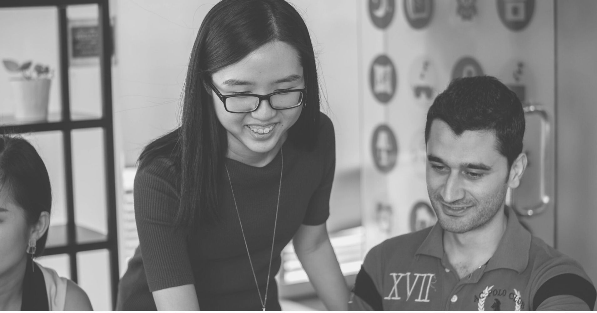 A young woman and a young man in an office setting looking down in same direction (as if looking at a paper or computer).